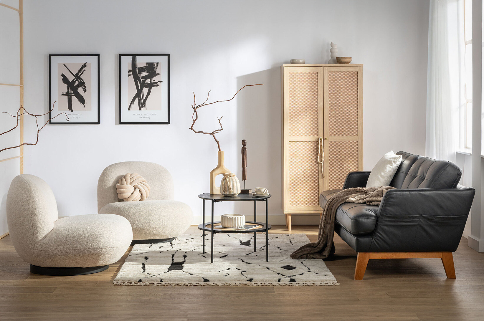 Nowoczesny salon z czarną skórzaną sofą, jasnymi fotelami boucle oraz szafą z rattanowymi frontami, elegancka aranżacja wnętrza w stylu japandi z naturalnymi dodatkami.
