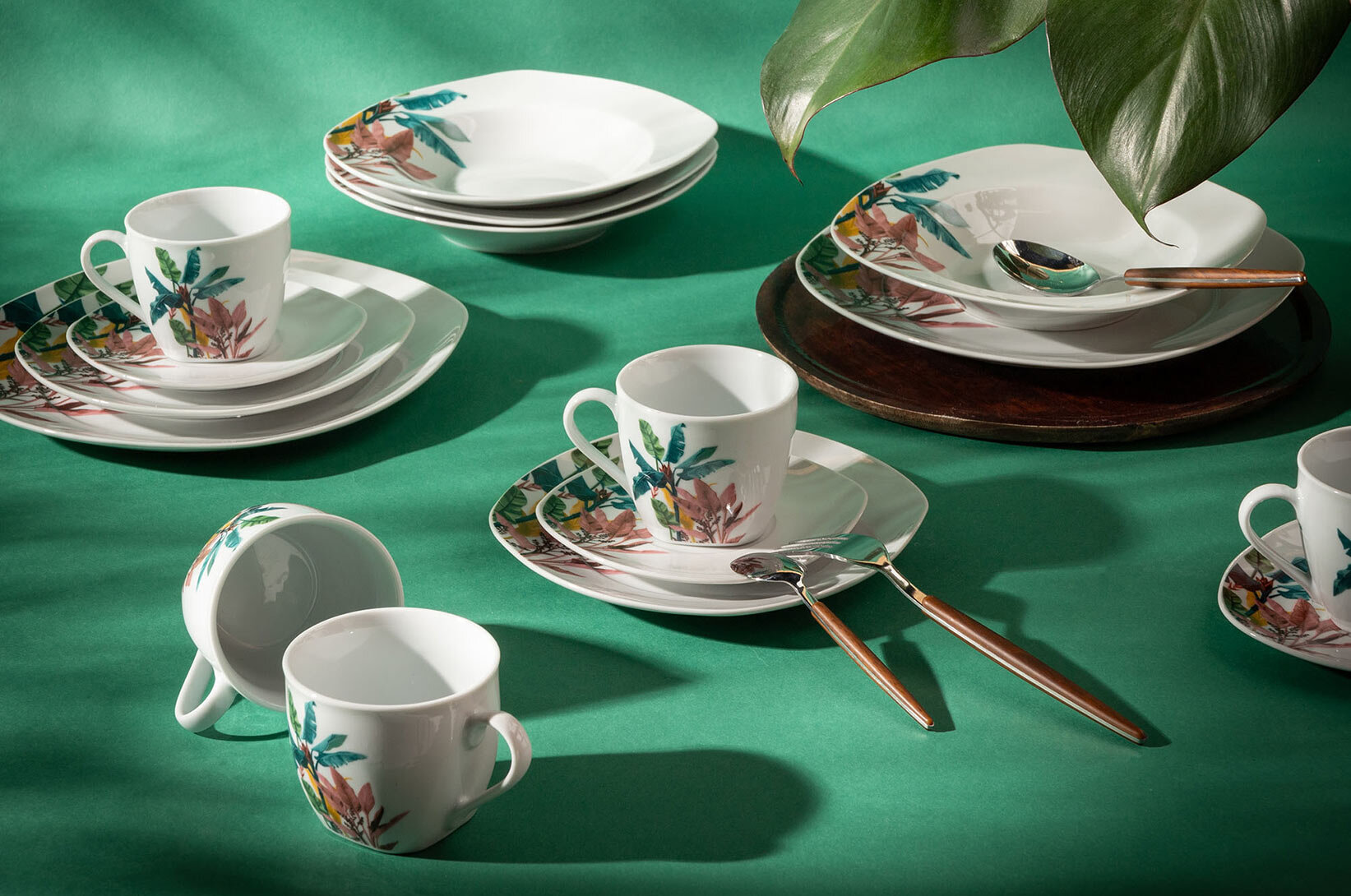 Porcelanowy serwis obiadowo-kawowy z tropikalnym motywem liści, komplet talerzy, filiżanek i misek do nowoczesnej jadalni oraz kuchni.