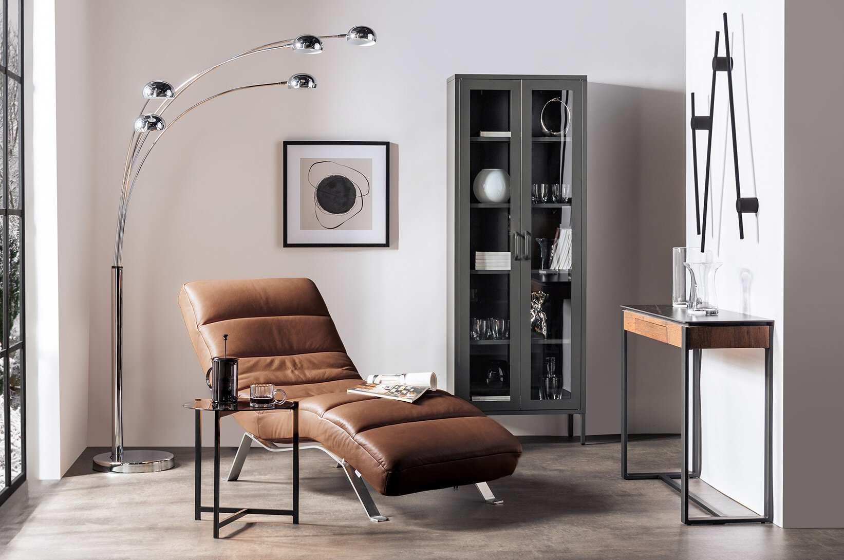 Brązowy fotel wypoczynkowy ze skóry, nowoczesna witryna i designerska lampa podłogowa, elegancka aranżacja salonu w odcieniach brązu i szarości.